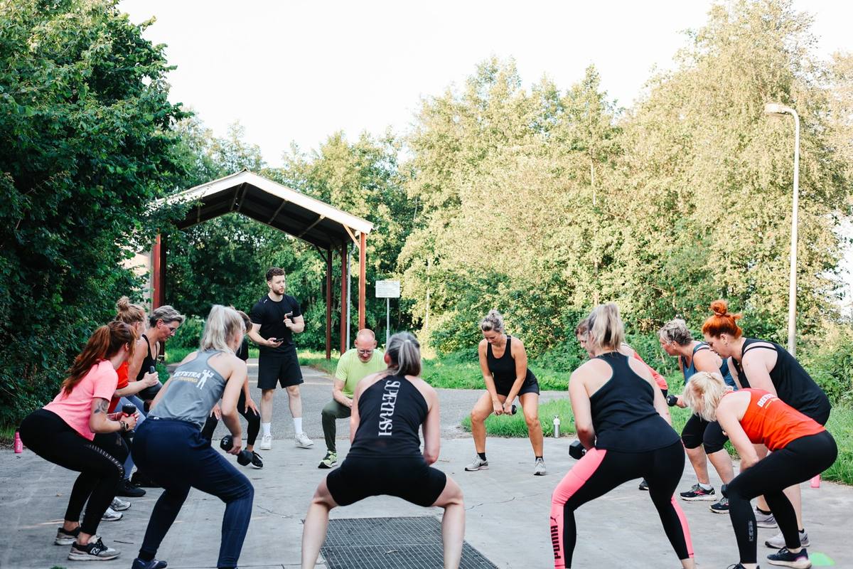Groep sporters traint buiten met gewichten onder begeleiding
