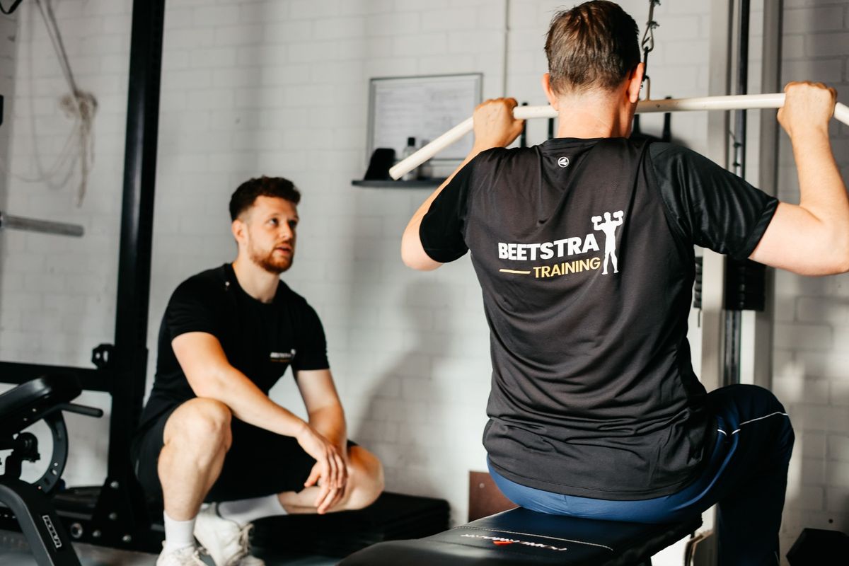 Trainer begeleidt een sporter bij een oefening in de gym